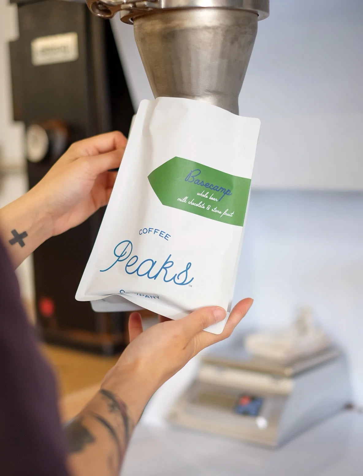 Person holding a 'Peaks' coffee bag with a coffee grinder in the background