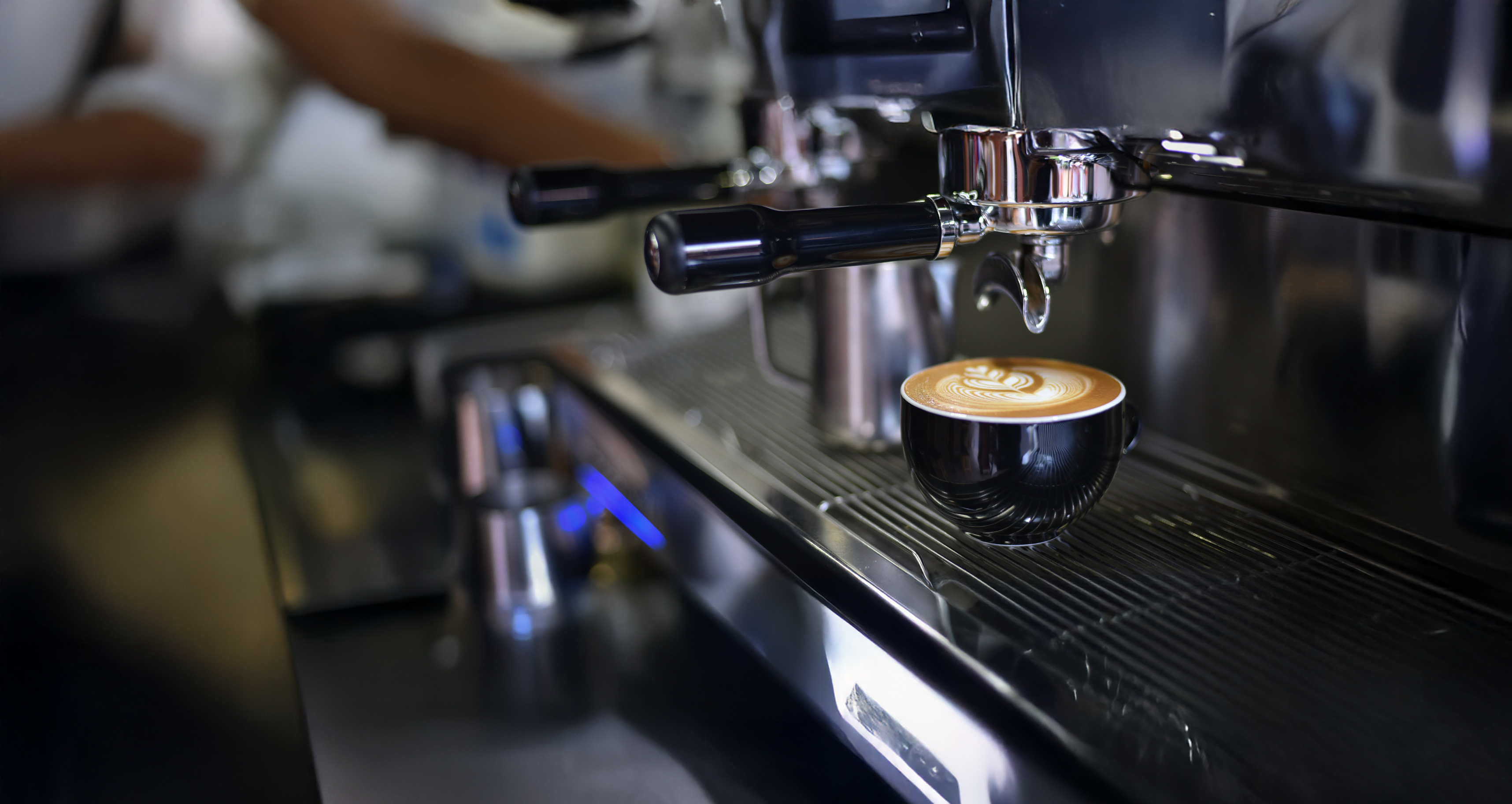 Espresso being brewed into a cup with a barista in the background