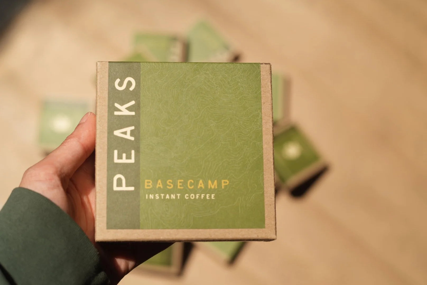 Hand holding a box of Peaks Basecamp instant coffee against a blurred background