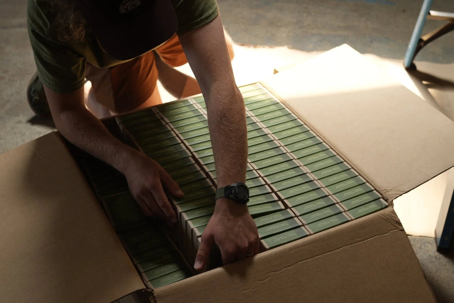 Person packing green boxes into a cardboard box
